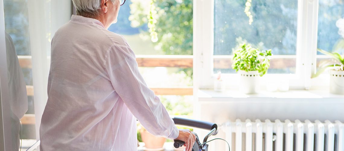 Elderly woman with a walker after a stroke looks out the window in the rehab clinic